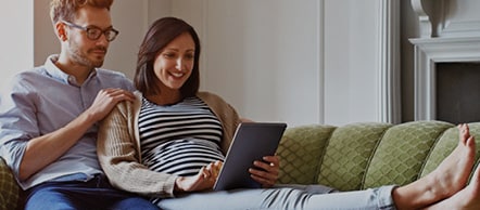 A man and a woman sitting on a sofa consulting a tablet.